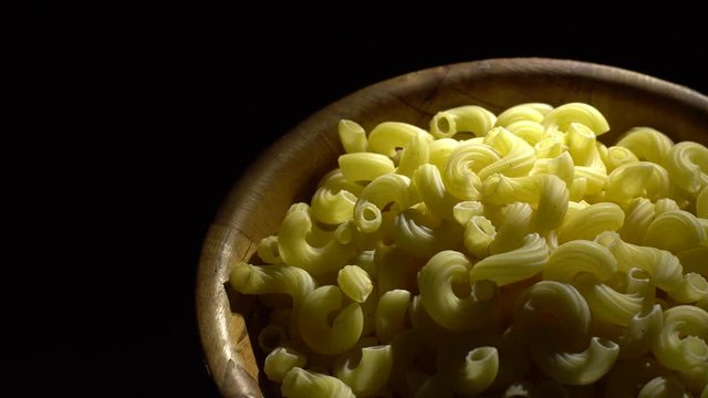 Raw macaroni in rotation. Elbow macaroni. Macaroni rigati close up.  Raw pasta  black background. Italian cuisine concept.