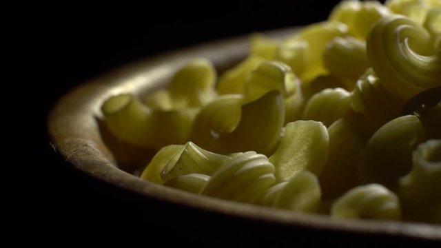 Raw macaroni in rotation. Elbow macaroni. Macaroni rigati close up.  Raw pasta  black background. Italian cuisine concept.