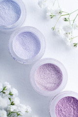 Fototapeta na wymiar flat lay jars of eye shadow in pastel spring colors on a white textured background with delicate white flowers gypsophila