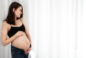Young pregnant woman stands near the window at home