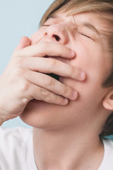 Fototapeta premium Boy yawns with his eyes closed, covering his mouth with his palm