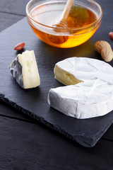 Camembert and honey on a black slate board. Soft cheese with mold and peanuts on a black background. Cheese and nuts on a stone board. Copy space