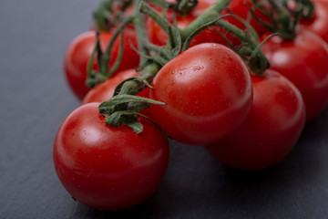Organic red cherry tomatoes on the vine and and natural stone background.