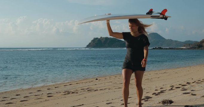 Surfer girl walking with board on sandy beach