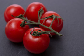 Organic red cherry tomatoes on the vine and and natural stone background.