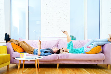 The guy and the girl are lying on the couch, discussing something in the smartphone.