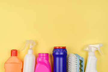 House cleaning supplies on  yellow background. Row of plastic bottles with cleaning liquid on wood, copy space on top.