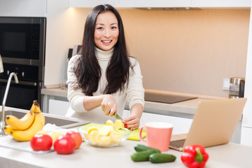 Obraz na płótnie Canvas Picture of young asian girl with mug and laptop standing at table with vegetables and fruits