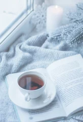 Photo sur Plexiglas Theé Nature morte d& 39 hiver confortable : tasse de thé chaud et livre avec plaid chaud sur le rebord de la fenêtre contre le paysage de neige de l& 39 extérieur.