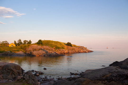 The rocky shore of the island of Suomenlinna and the sea view in the Gulf of Finland at sunset on a summer evening in Finland.