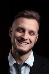 Close up portrait of elegant young fashion man in tuxedo laughing.on black background