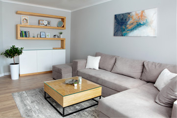 Grey corner couch with three pillows standing in bright living room interior with painting and carpet.Lightning off.