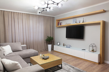 Grey corner couch with three pillows standing in bright living room interior with painting and carpet.Lightning on