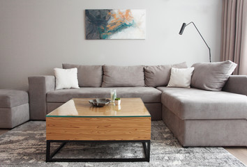 Grey corner couch with three pillows standing in bright living room interior with painting and carpet.Lightning off.