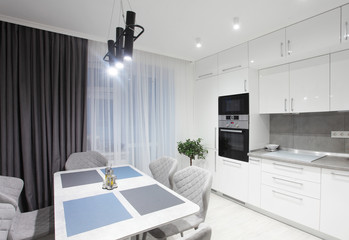 White kitchen interior with grey chairs,moss on the wall in new luxury home with lights on.