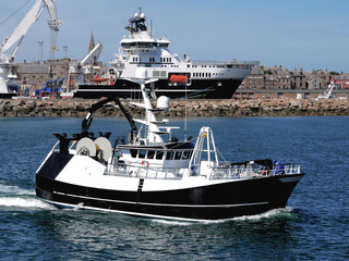 Naklejka premium Fishing vessel underway departing fishing harbour for fishing grounds.