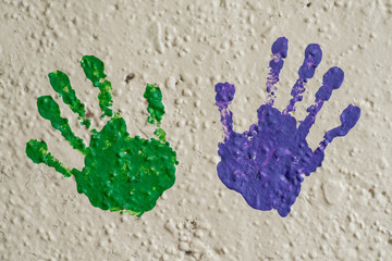 Color hand prints painted on a white concrete wall.