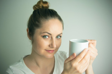 The morning's awakening. Young woman in the morning, holding cup of tea indoors. Portrait of young girl, woman with cup of hot drink.