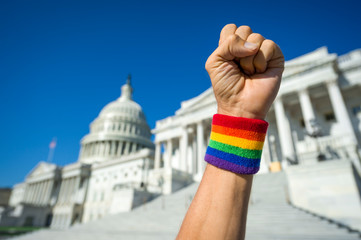Hand wearing gay pride rainbow wristband making a power fist gesture in front of the US Capitol...