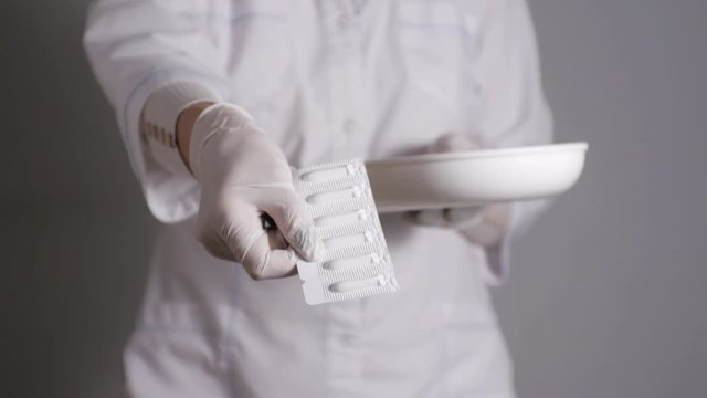 Female doctor giving medication. Young medical professional gives suppositories in a blister taking from kidney dish. Slow motion.