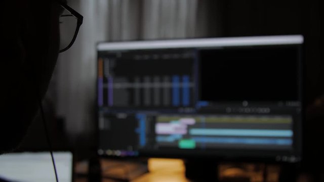 Young Man using Computer, Editing a video in editing software, Shot from behind.