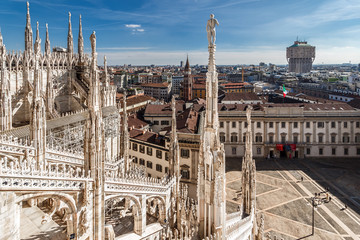Fototapeta premium Widok z góry z dachu katedry Duomo di Milano z marmurowymi posągami na miasto i Pałac Królewski Palazzo Reale na placu Piazza del Duomo. Mediolan, Włochy.