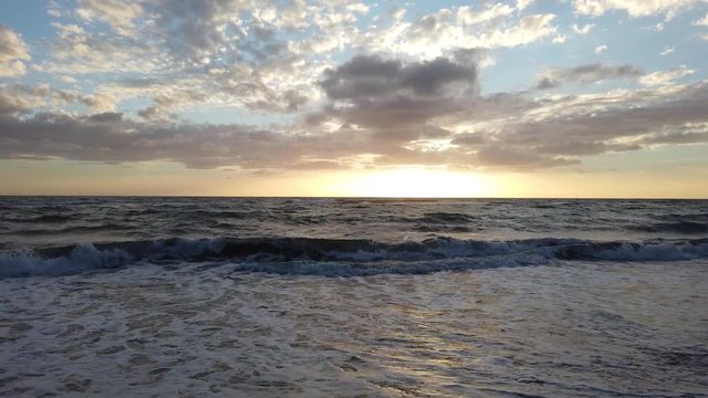 Awesome golden hour sunset at beach with fantastic sky with altocumulus stratiformis and ocean waves breaking on shoreline with sunbeams reflections on rough sea foamy water