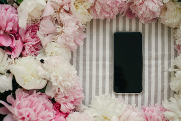 Phone with empty screen and peonies frame flat lay on rustic table cloth. Space for text. Blogging and instagram concept. Greeting card mockup. Happy mothers day.