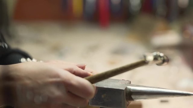 Woman hands placing the gold ring on a metal mandrel and using a mallet to round the shank. Blurred background. Close-up concept