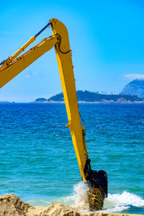 Backhoe removing sand from the beach and throwing in the sea to unclog the passage