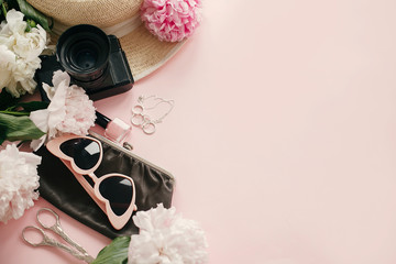 Obraz na płótnie Canvas Stylish feminine flat lay with pink peonies, hat, photo camera, retro sunglasses, jewelry and nail polish on pastel pink paper with copy space. International Women's Day. Hello spring