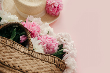 Straw hat and rustic bag with white and pink peonies on pastel pink paper.  Hello spring image with copy space. Summer vacation concept. International Women's Day. Happy mothers day