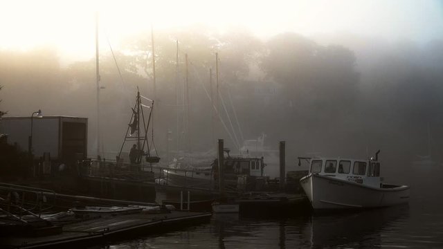 Lobster fishing boat getting ready to set sail in the early morning light at sunrise in a foggy and quaint New England harbor.