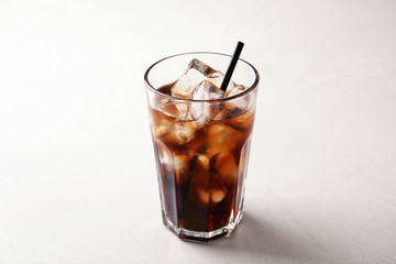 Glass of refreshing cola with ice on white table
