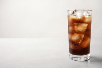 Glass of refreshing cola with ice on light table. Space for text