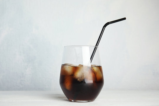 Glass of refreshing cola with ice cubes and straw on table