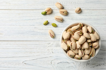 Organic pistachio nuts in bowl on wooden table, top view. Space for text