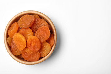 Wooden bowl of dried apricots on white background, top view with space for text. Healthy fruit