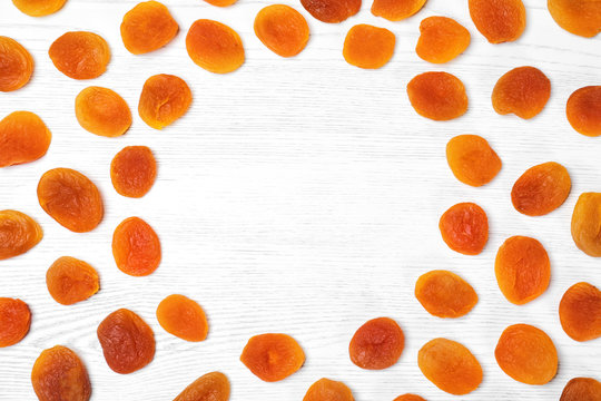 Frame made of dried apricots on white wooden table, top view with space for text. Healthy fruit