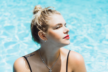 Young beautiful blonde woman with a good figure with red lips make-up posing in a pool of blue...