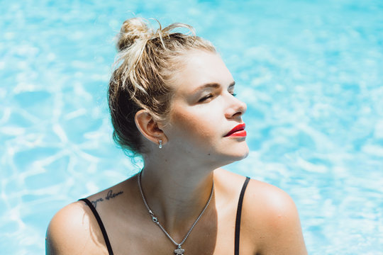 Young beautiful blonde woman with a good figure with red lips make-up posing in a pool of blue water. Outdoor portrait close up. 