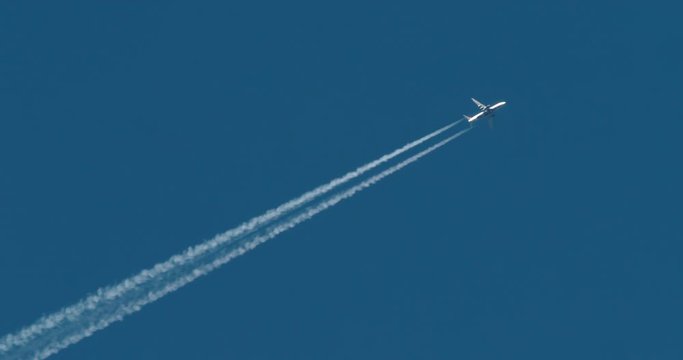 Jet airplane flying overhead in clear blue sky and leaving nice contrail. Camera tracks the plane smoothly as it flies through the sky.