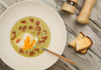Asparagus cream soup. Delicious homemade green asparagus cream soup with poached egg and ham on a rustic wooden background