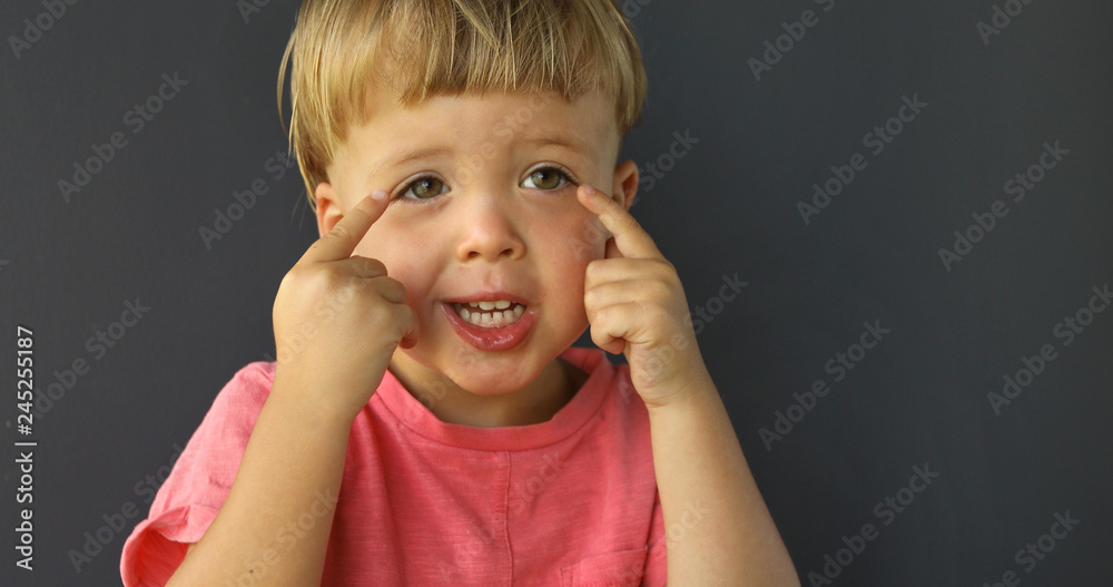 Wall mural boy points his fingers of both hands on his eyes