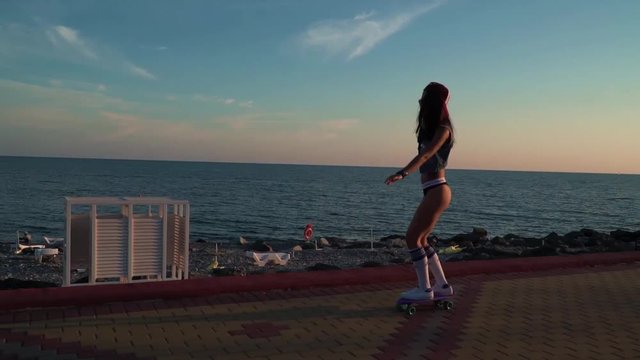 Sporty tan young brunette slowly surf skateboard on the seaside in a sunset low lights