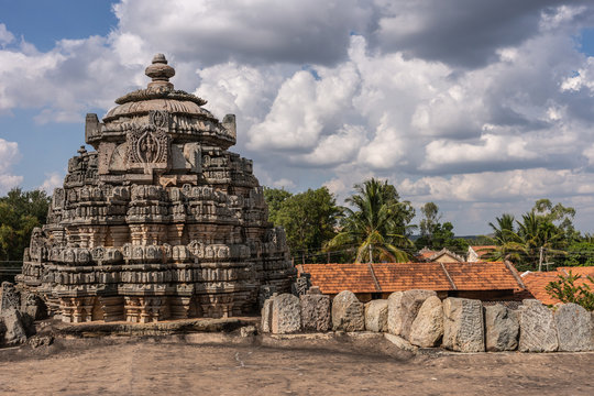 Belavadi, Karnataka, India - November 2, 2013: Veera Narayana Temple. One of three brown-stone Vimana towers of the complex under cloudscape. Shot from upon roof. Green vegetation and red roofs.