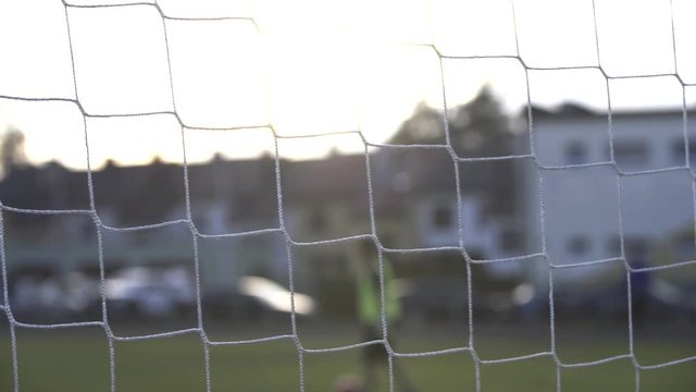Football goal post net minutes before the match, with a authorized person maintaining the field in the background
(close up shot) (depth of field)