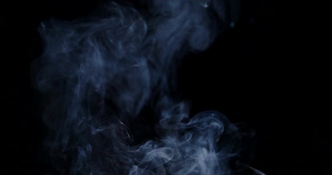 Bluish cloud of smoke rises in front of a black background in slow motion