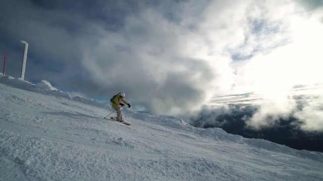 Slow motion of a female skier riding through the mountains edge in fornt of fascinationg XXXX clouds.
