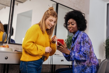 Beautiful dark-skinned stylist in an orange top showing a picture to her client